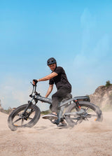 a man wearing a helmet rides an engwe x26 folding electric bicycle on the sand